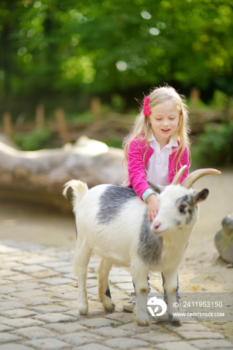 可爱的小女孩在宠物动物园抚摸和喂养山羊。孩子在阳光下与农场动物玩耍