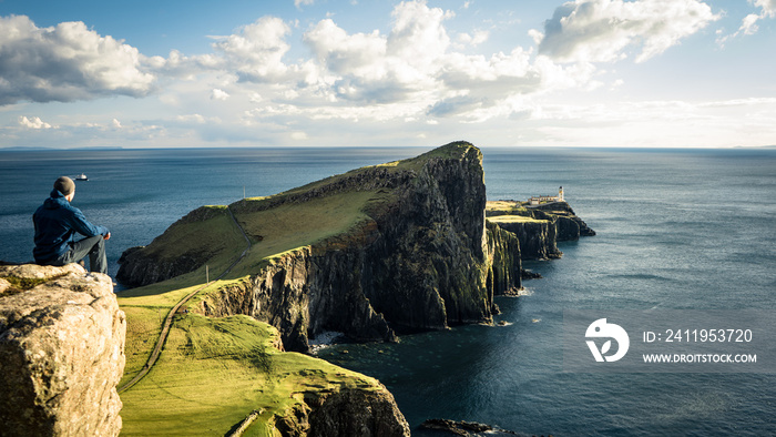 Tourist stand alone view with famous Cliffs of Neist Point Cape and lighthouse during sunset. Popula