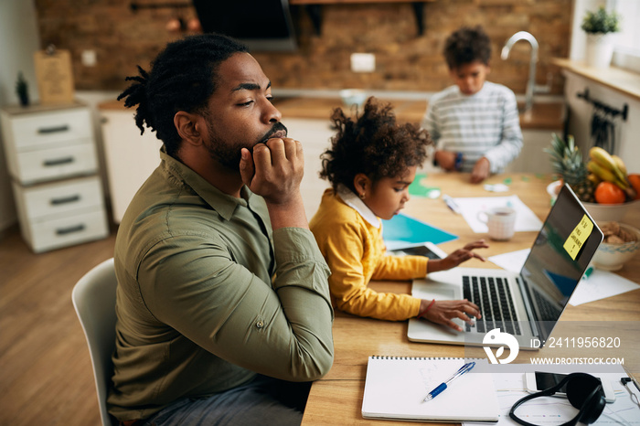 Pensive African American working father with his children at home.