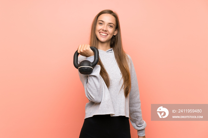 Happy Young sport woman over isolated pink background making weightlifting with kettlebell