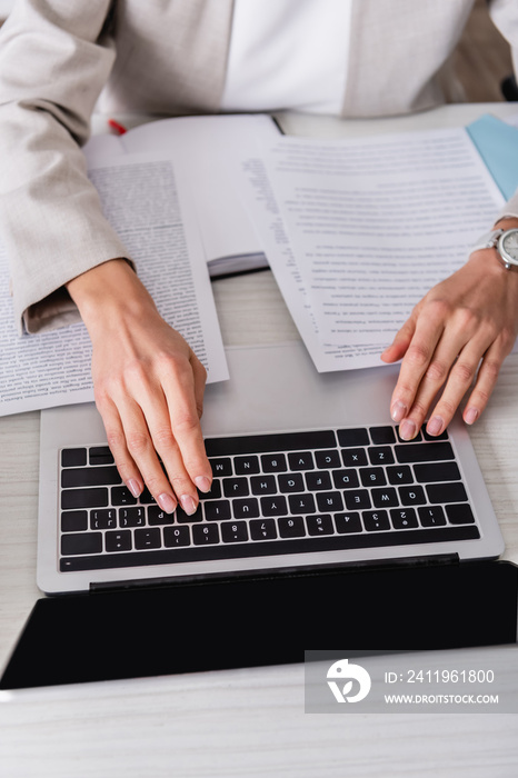 partial view of translator typing on laptop near documents in office