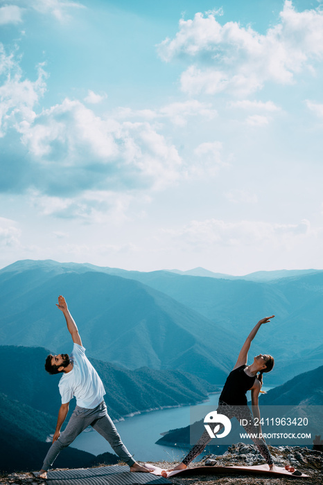 Attractive couple practicing yoga at mountain peak