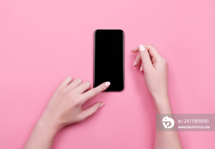 Top view of a woman hand using phone on pink pastel background.