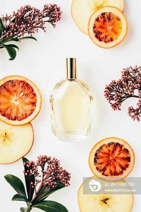 top view of glass bottle of perfume surrounded with fruits and flowers on white