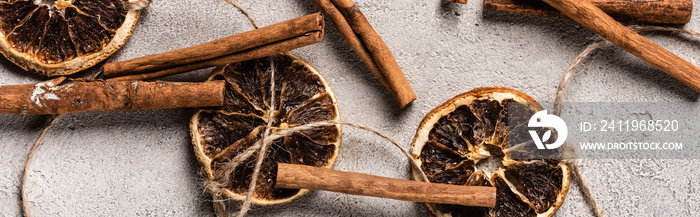 Panoramic shot of dried orange pieces and cinnamon sticks on grey background