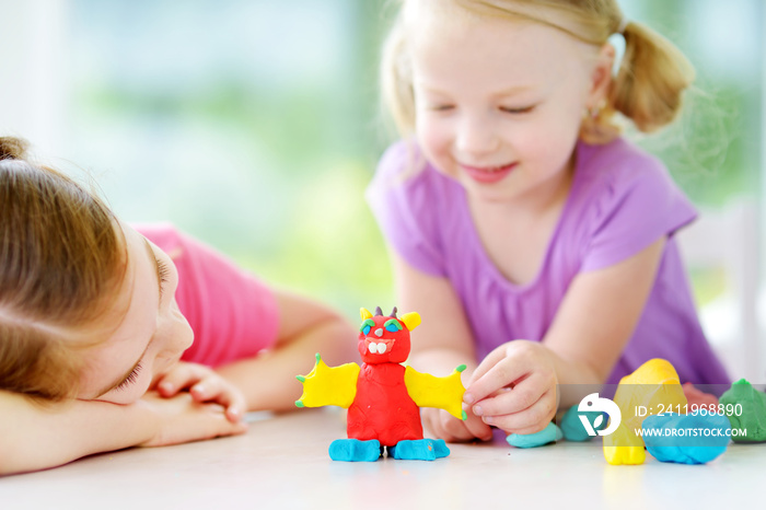 Two cute little sisters having fun together with colorful modeling clay at a daycare. Creative kids 