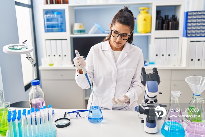 身穿科学家制服的年轻西班牙妇女在实验室使用移液管工作