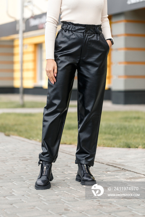 街上穿着黑色皮裤的年轻女子。女式时尚人造革长裤