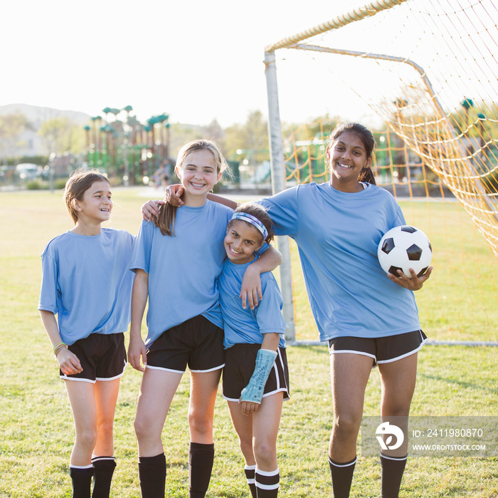 Smiling soccer players standing on grassy field against sky during sunny day