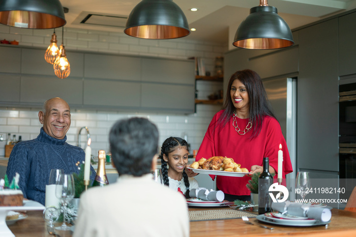 Smiling woman serving roasted turkey to family at table