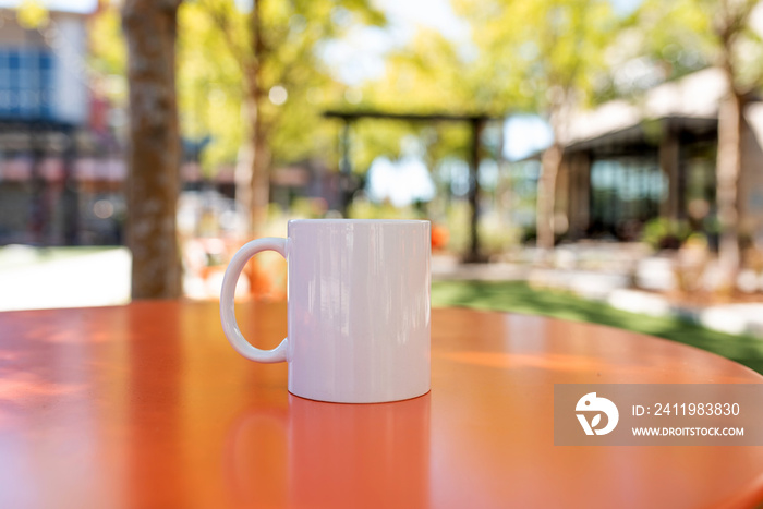 White blank coffee mug on the table outside the coffee shop on a sunny day.