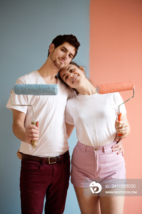 Couple standing in front of freshly painted wall with rollers