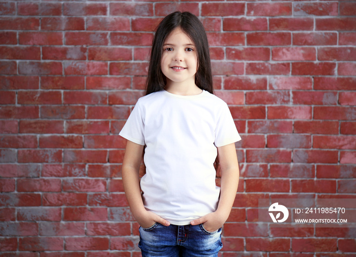 Little girl in blank white t-shirt standing against brick wall