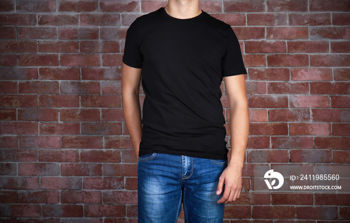 Handsome young man in blank black t-shirt standing against brick wall, close up