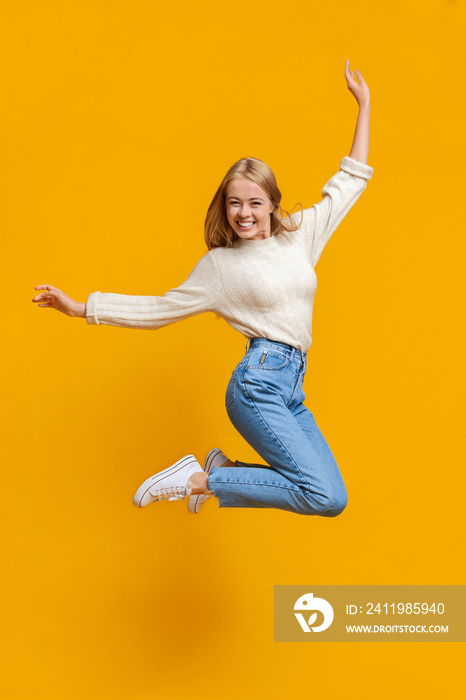 Teenage girl having fun jumping in air on orange background