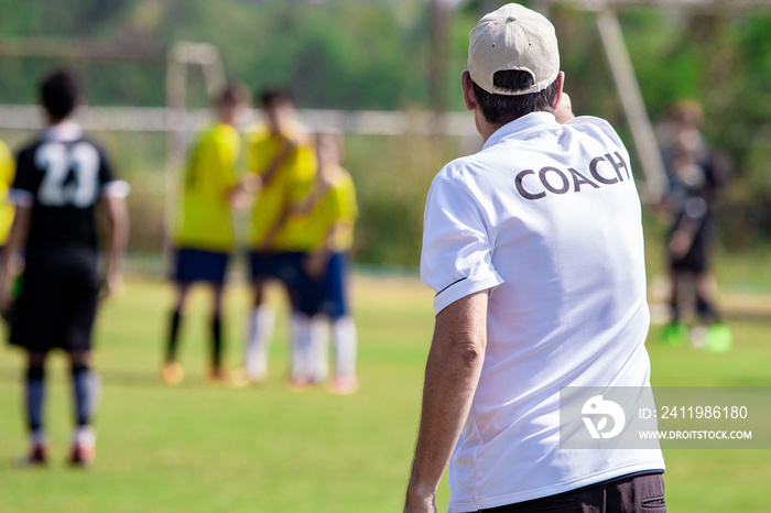 Back of football coach wearing white COACH shirt at an outdoor sport field coaching his team during 