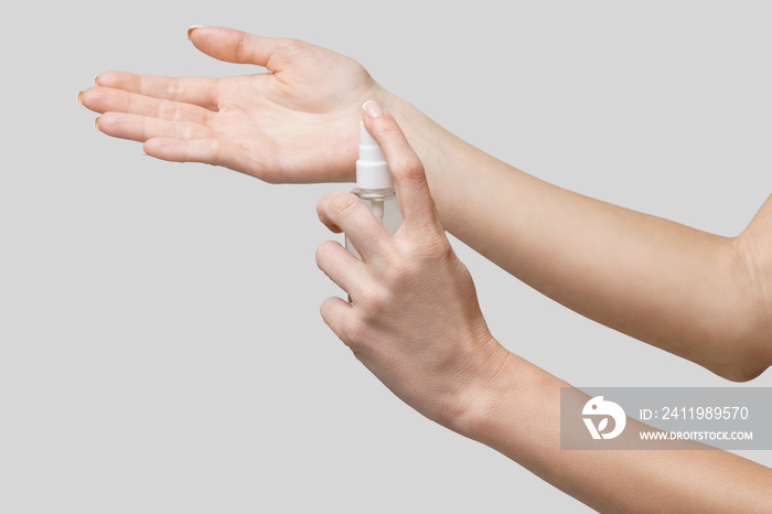 Female hands using hand sanitizer spray dispenser over light grey background