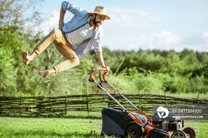 一个顽皮的男人在用汽油割草机割草时跳跃，在草坪上享受园艺过程
