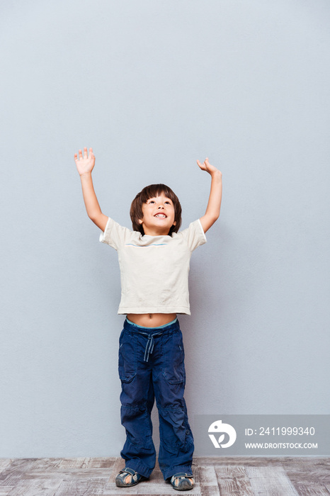 Full length of cheerful little boy standing with raised hands