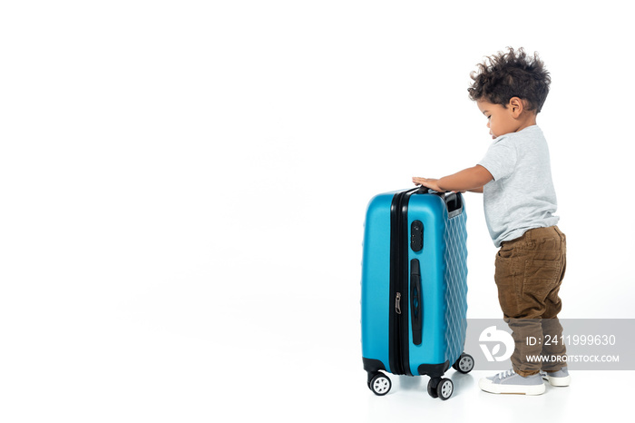 full length view of toddler african american boy standing near travel bag on white