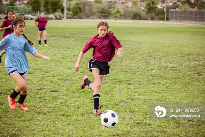 Full length of sporty girls running while playing soccer on field during competition