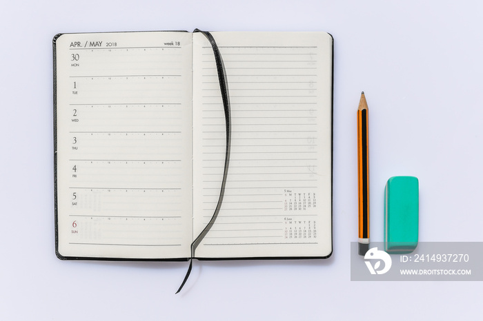 A diary open with instruments for writing. Pencil, eraser and notebook on white background. Close up of a wooden pen orange and black, an eraser green and a booklet black.