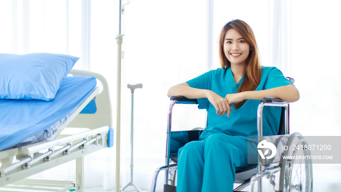 Portrait shot of young happy healthy Asian female patient in blue green hospital uniform sitting alo