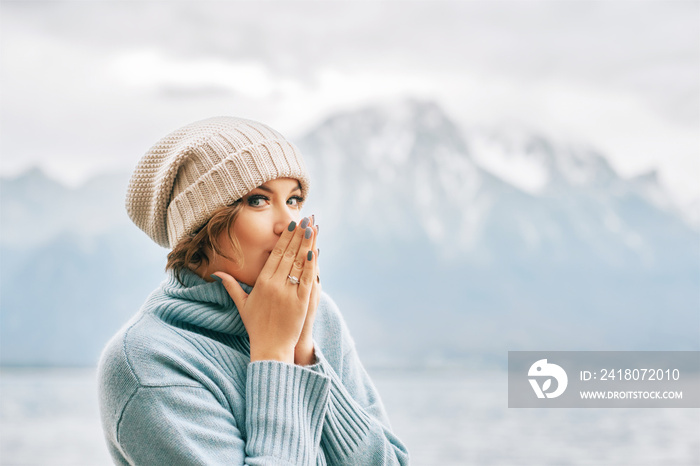 Outdoor portrait of beautiful young woman wearing blue pullover and hat, cold weather in mountains