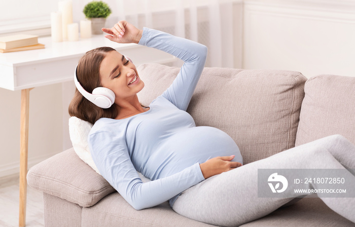 Happy Expectant Girl In Earphones Enjoying Music Lying On Sofa