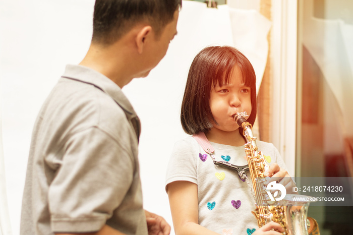 父亲教女儿吹萨克斯。父亲训练亚洲小女孩吹萨克斯乐器。亚洲