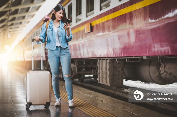 woman travel with luggage using smartphone at train station platform