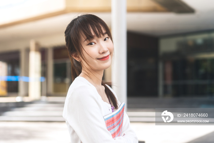 Portrait of young adult asian college student woman with notebook on day in the city.