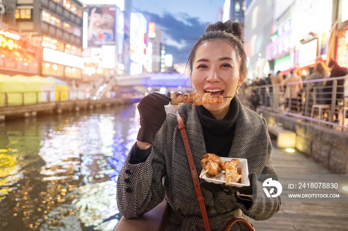 Young woman tourists enjoy eating street food in walking at street shopping center Dotonbori in Osak