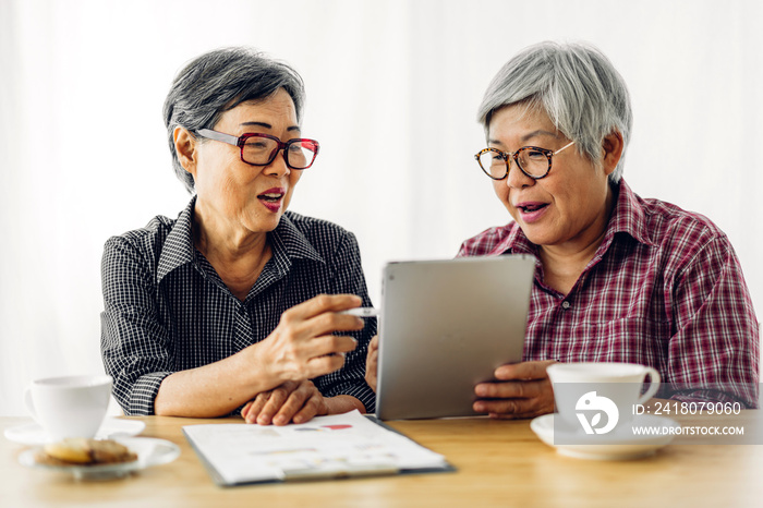 Portrait of two friend happy senior adult elderly asia women smiling and working with tablet compute