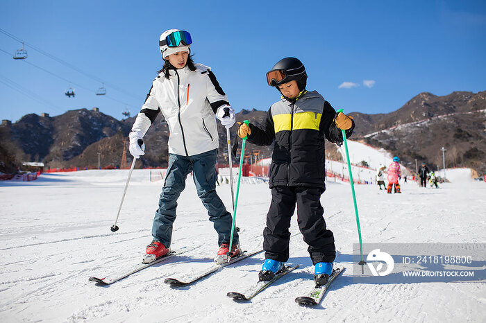 小男孩跟着教练在户外学滑雪