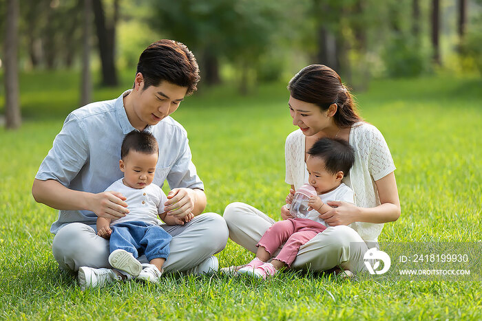 年轻父母在公园陪龙凤胎宝宝玩耍