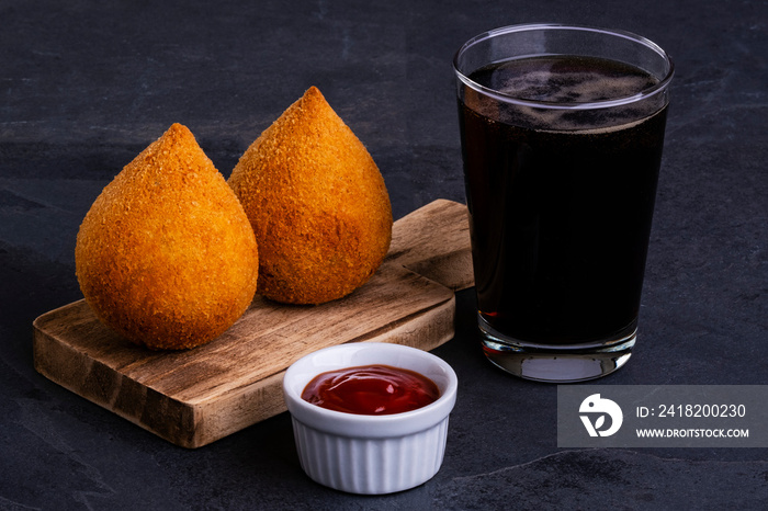 Traditional fried coxinha stuffed with chicken and a glass of cold soda