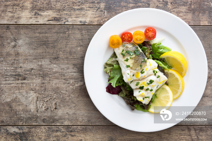 Fried cod fillet and salad in plate on wooden background