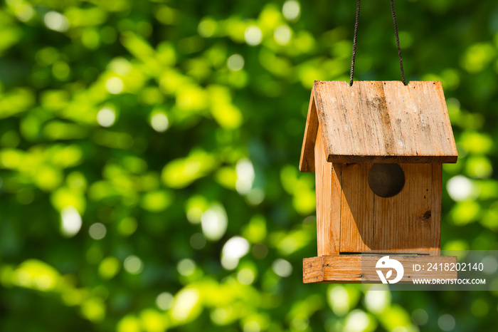 Old wooden birdhouse hanging with ropes. On a green blurred background