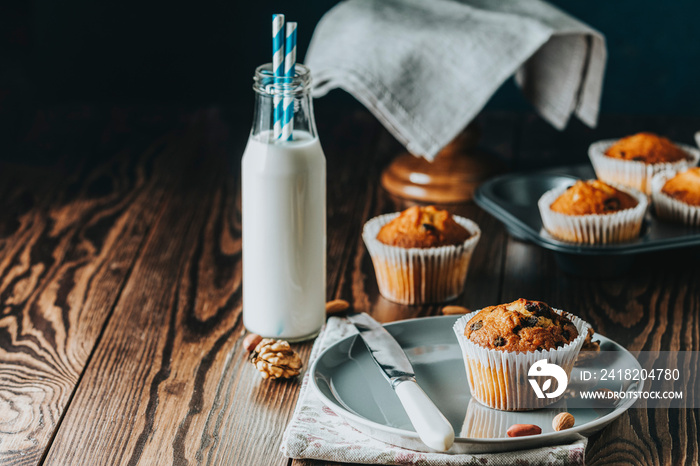 Vanilla caramel muffins in paper cups and bottles of milk on dark wooden background.