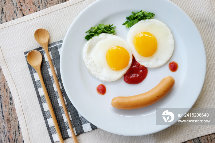 Top view of fried egg smile face on white plate with wooden spoon on white fabric table, breakfast s