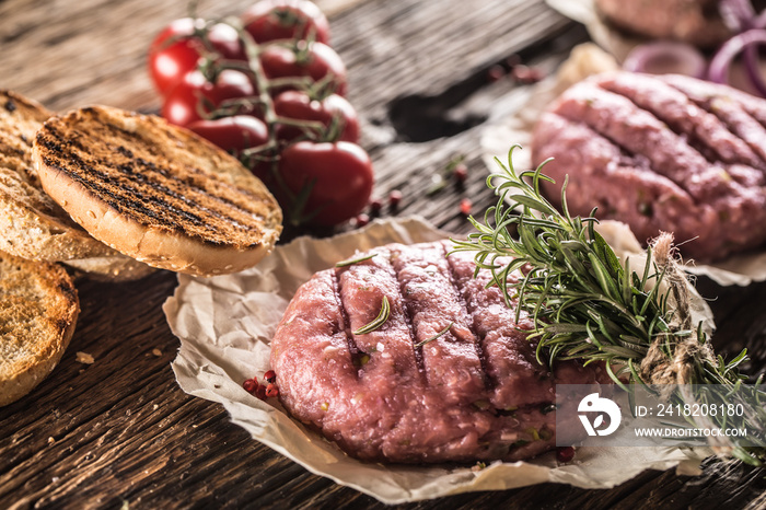 Raw burgers on wooden table with onion tomatoes herbs and spices