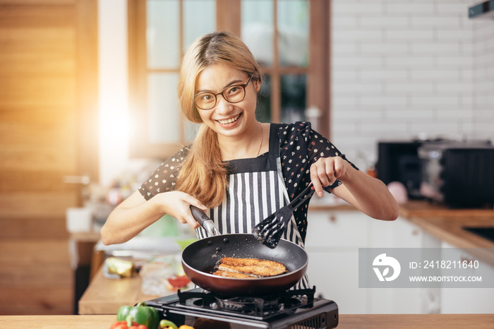 幸福的年轻女人在现代厨房里微笑。美丽的亚洲女人站在厨房里做饭