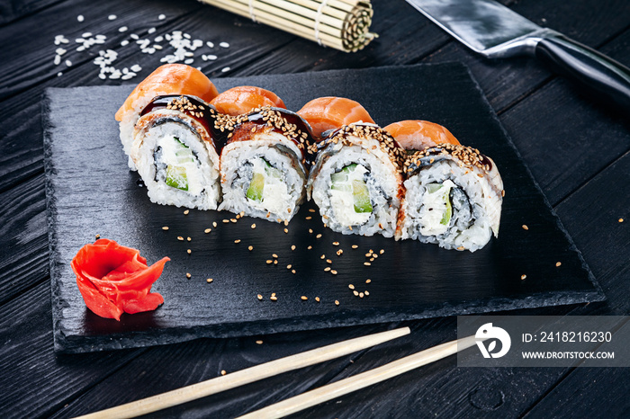 Served sushi rolls on black stone with chopsticks. Close up view on sushi on dark background. Tradit