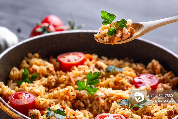 Full pan of homemade delicious pilaf with chicken, fresh parsley and ripe vegetables close up