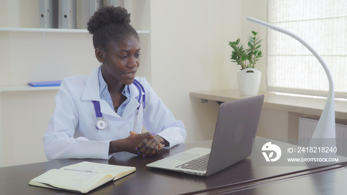 Afro american doctor chatting online with client. Professional woman wearing in white coat on her ne