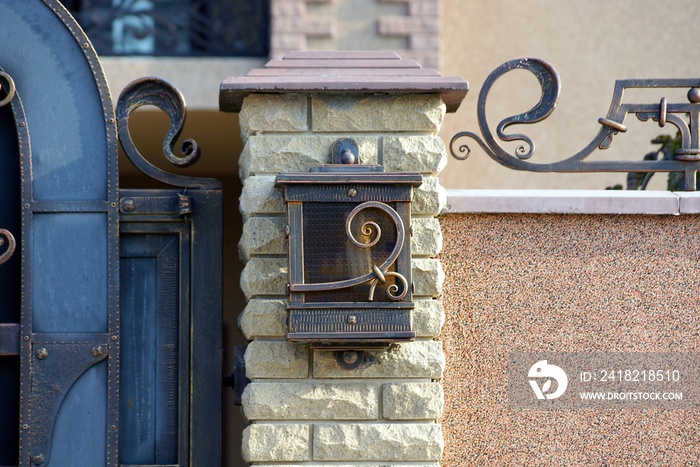 一个棕色邮箱，由玻璃和金属制成，砖栅栏上有锻造图案