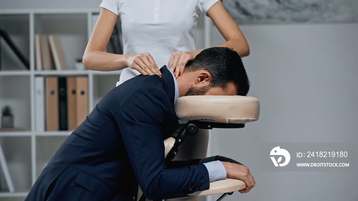 Masseur doing neck massage to businessman in suit in office