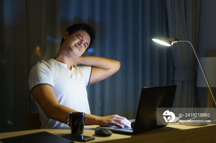 Asian man are stretch lazily while working long hours in front of a computer in late night in living