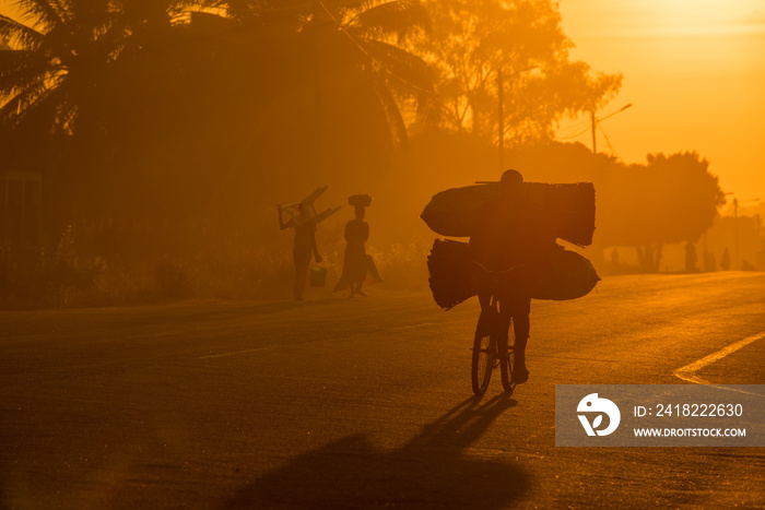 早上日出时，一名莫桑比克骑自行车的人沿着柏油路面，背着大包煤去市场